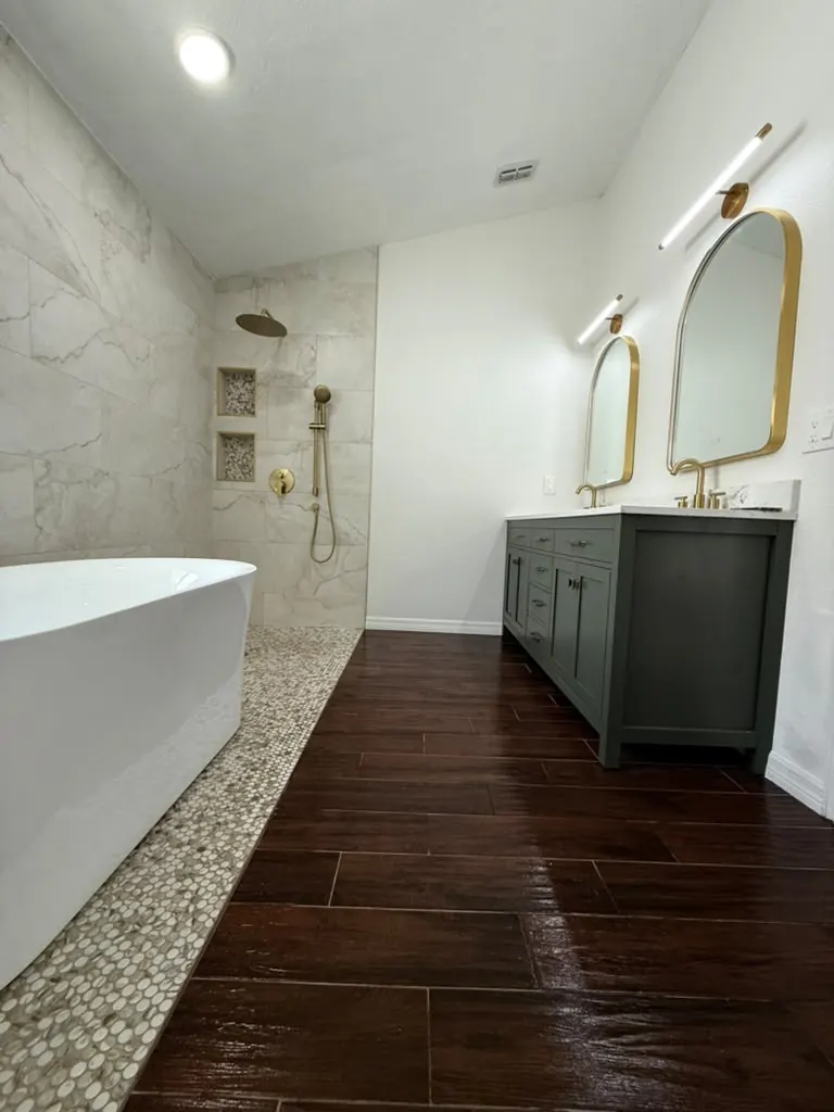 Primary bathroom with a curbless walk-in shower, marble-look porcelain, freestanding tub and a green double vanity with brass fittings
